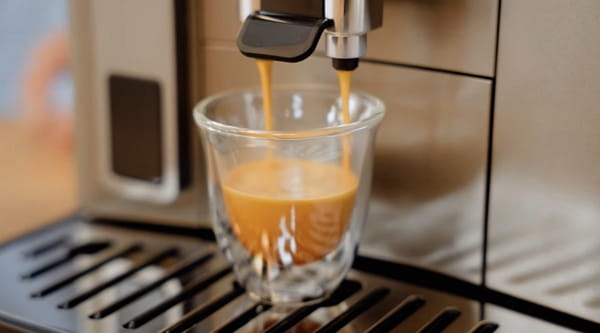 Espresso pouring from the De’Longhi Magnifica Evo dual spouts into a glass with crema forming